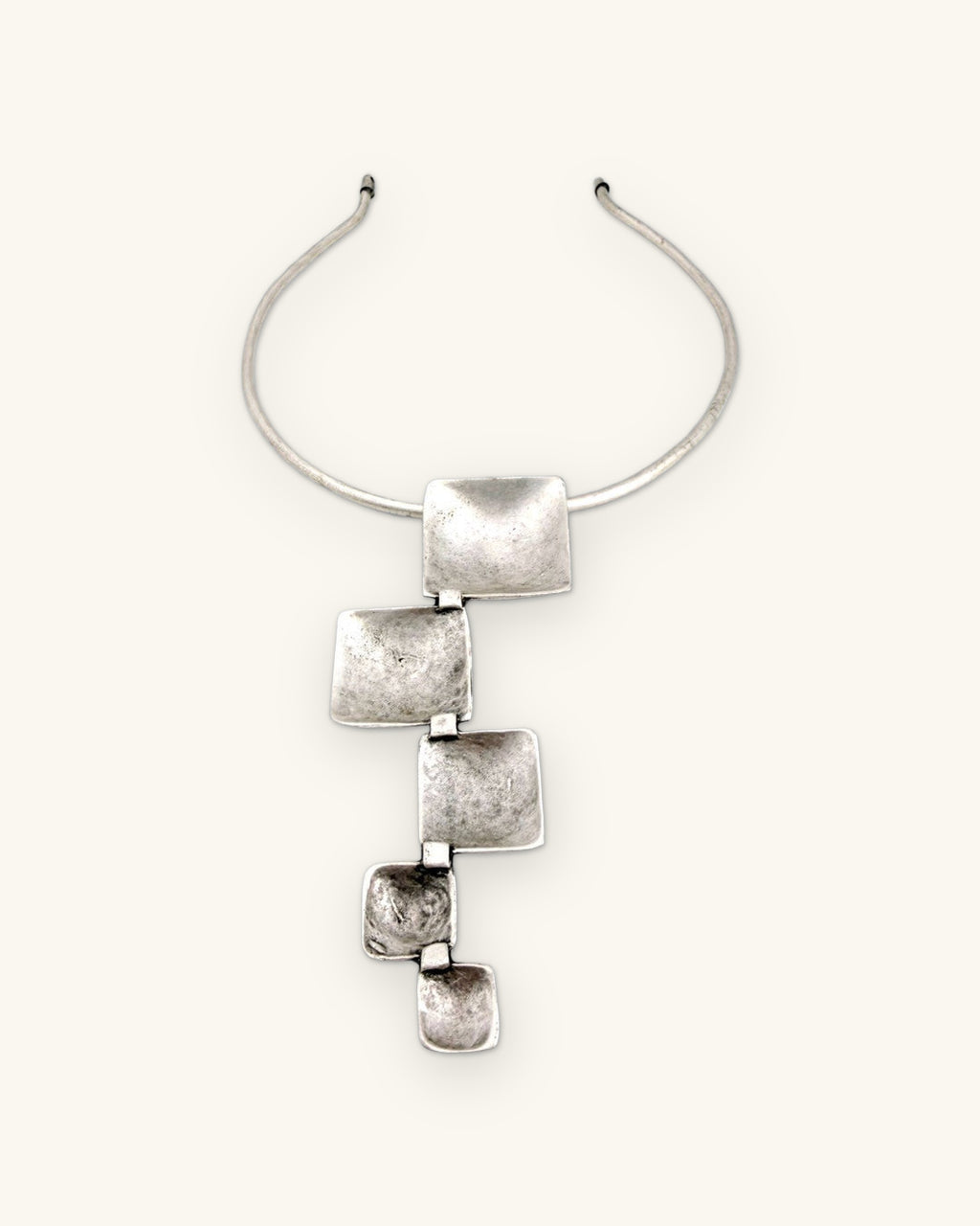 Close-up of the textured, cupped silver-tone squares linked below the rigid collar, shown on a sand background