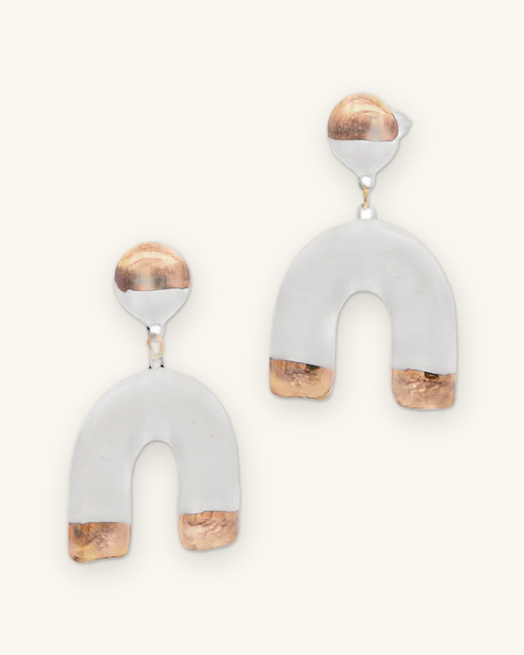 Pair of gold-dipped white ceramic horseshoe drop earrings with round gold and white studs, shown on a sand background