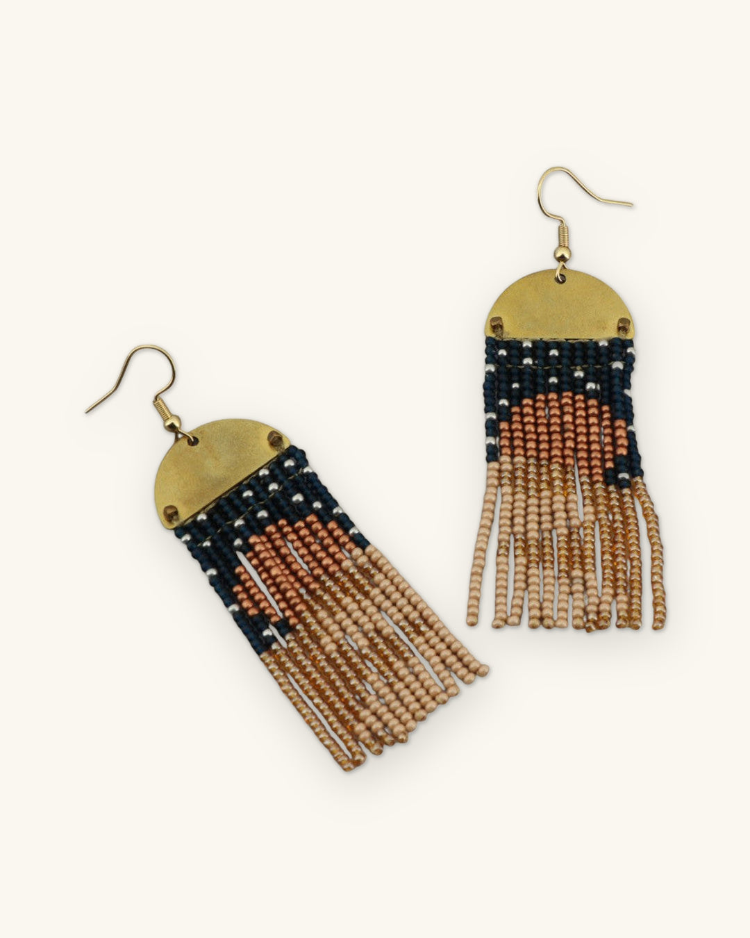 Pair of brass half-moon fringe earrings showing the copper sun motif fading into sand-colored fringe, shown on a sand background