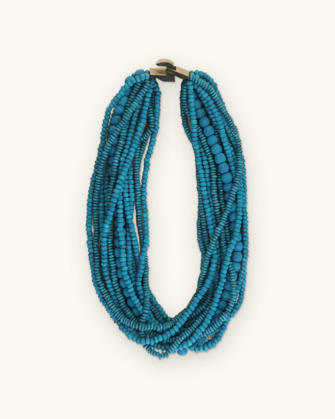 Twisted turquoise wood bead multi-strand necklace laid flat on a cream surface, shown on a sand background