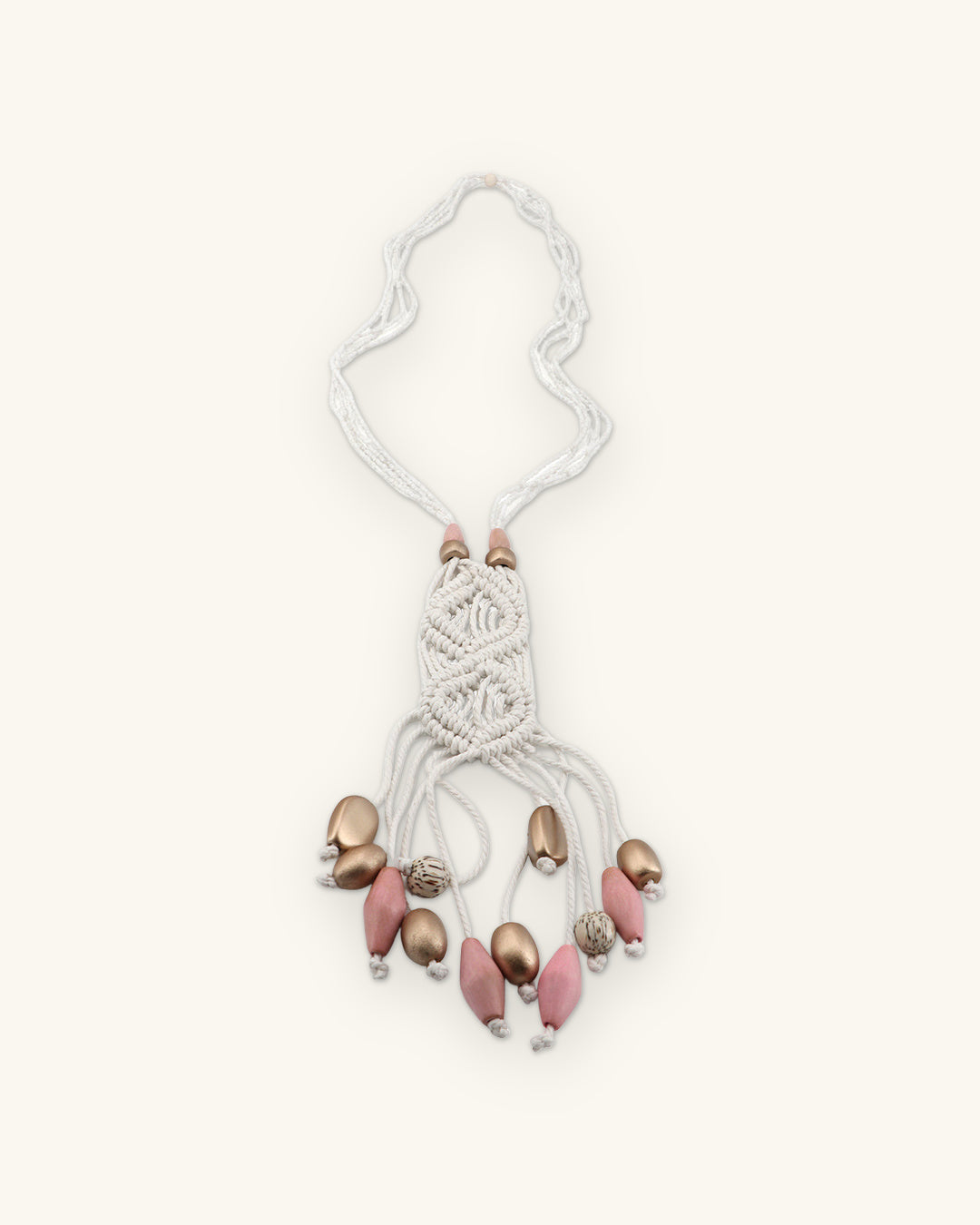 Full view of the ivory macramé pendant on seed bead strands with a fringe of pink and metallic wood beads, shown on a sand background