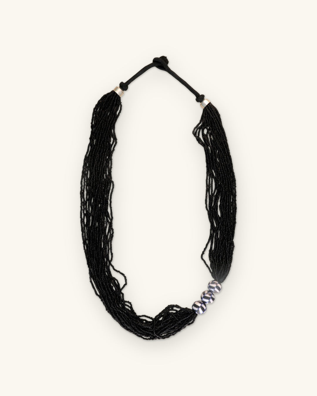Full view of the black multi-strand seed bead necklace with knotted black cord closure, shown on a sand background