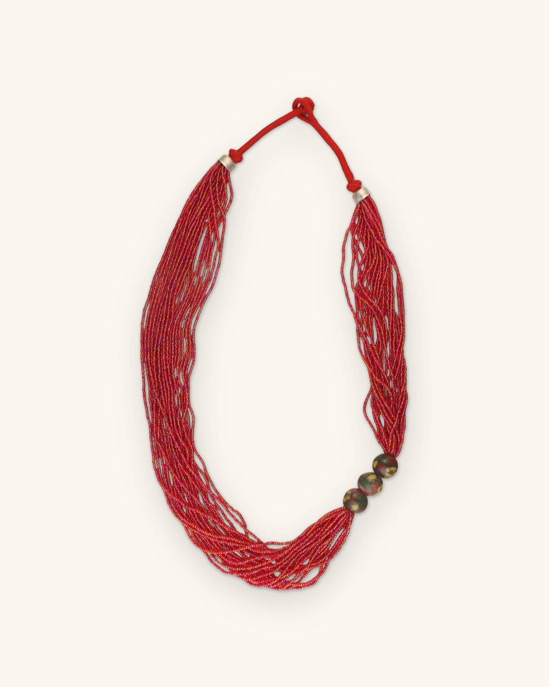 Full view of the red seed bead necklace with knotted red cord closure and silver-tone caps, shown on a sand background