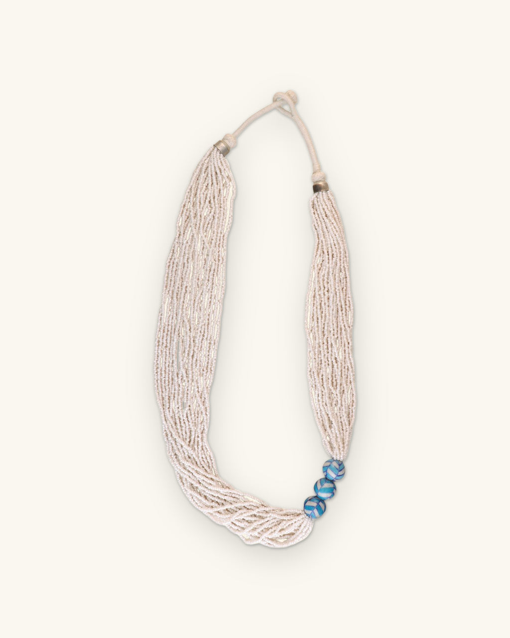 Full view of the white multi-strand seed bead necklace with knotted cord closure, shown on a sand background