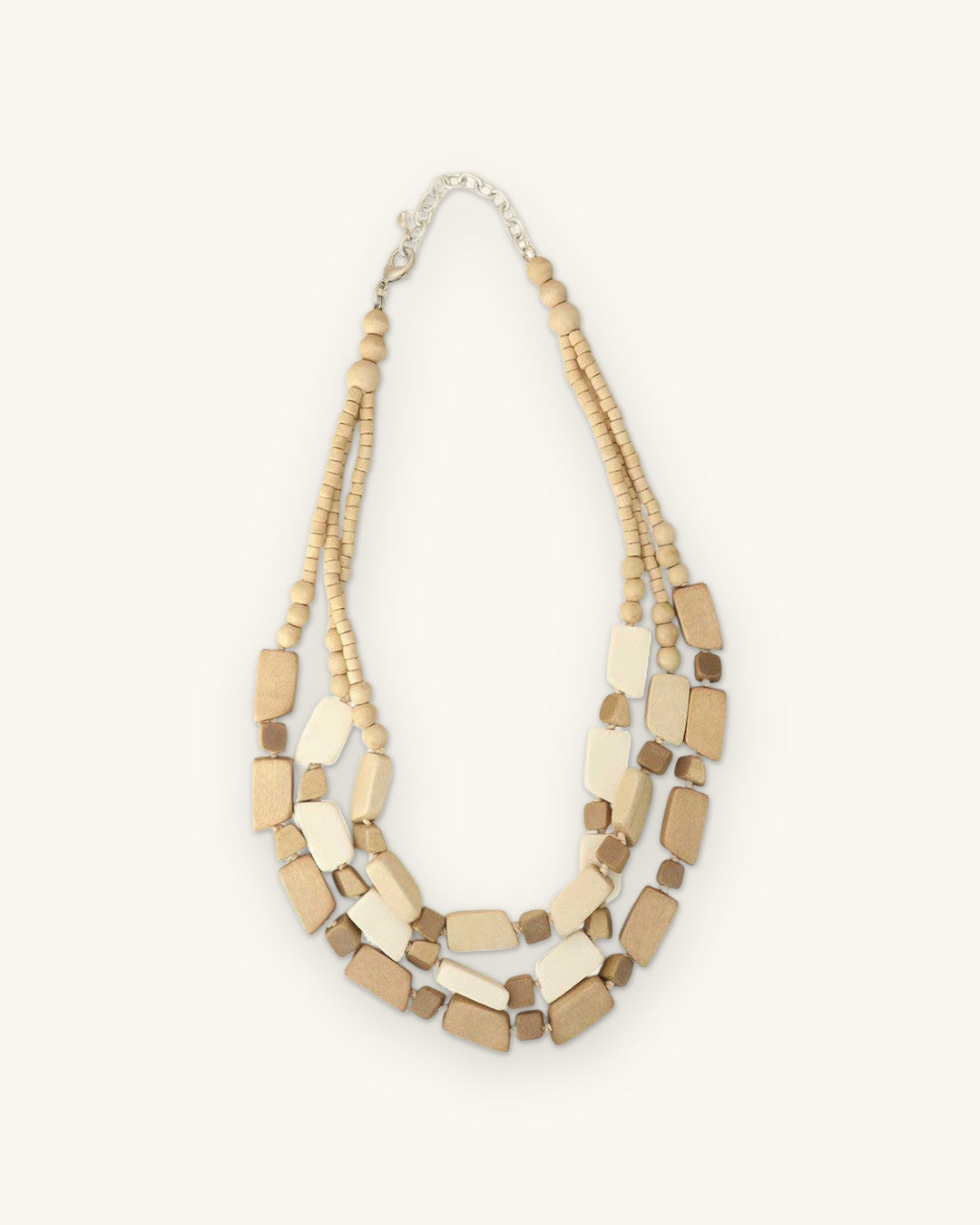 Full view of the three-strand cream and tan wood bead necklace with silver-tone chain closure, shown on a sand background