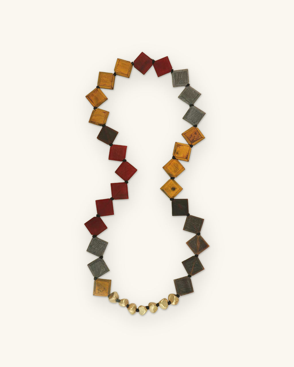 Long necklace of diamond-set dyed horn beads in red, mustard and gray with a brass bead section, made in India, shown on a sand background