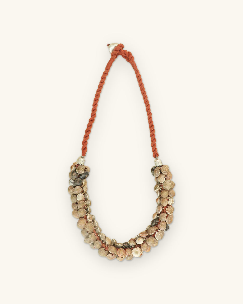Natural shell cluster necklace on a rust twisted cord with silver-tone end caps, laid flat, shown on a sand background