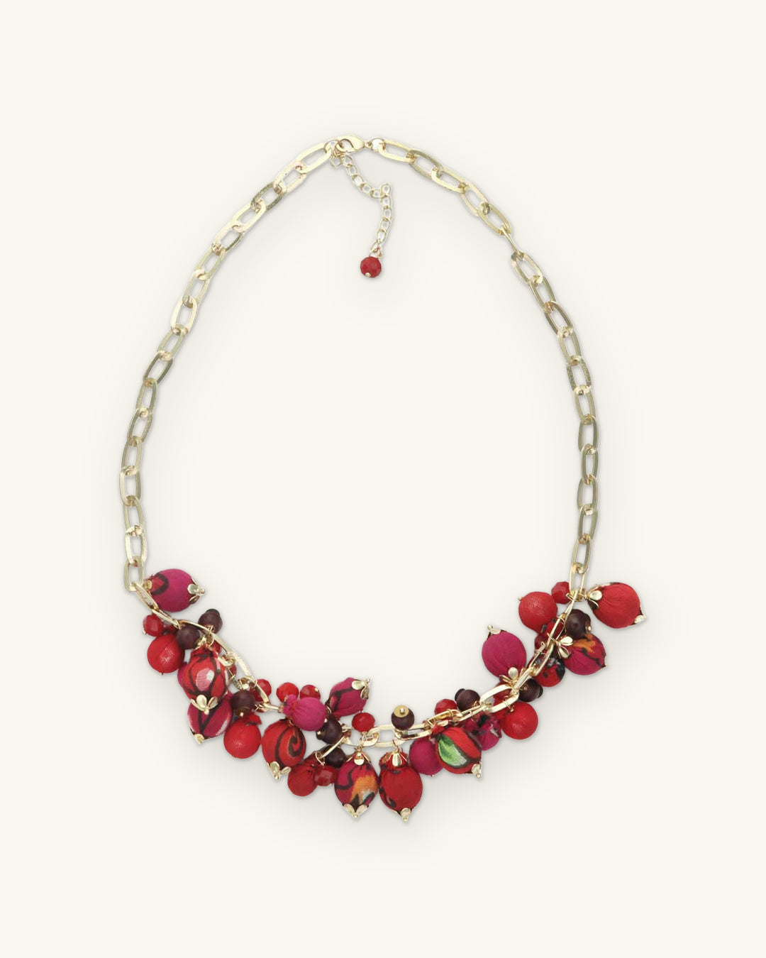 Full view of the red and magenta fabric bead bib necklace with extender and red bead drop, shown on a sand background