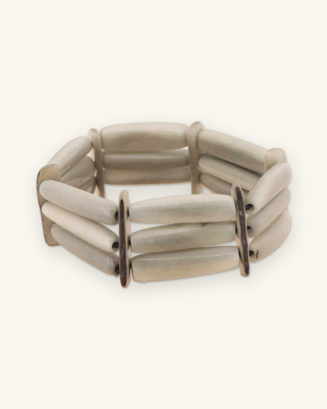Three-row pale gray-green tagua nut tube bracelet with dark spacer bars, dyed with organic vegetable dye in Ecuador, shown on a sand background