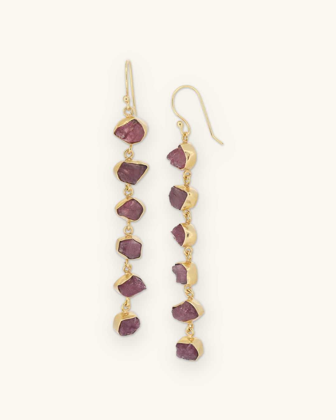 Raw pink tourmaline six-stone drop earrings bezel-set in gold-plated brass on fish-hook wires, made in India, shown on a sand background