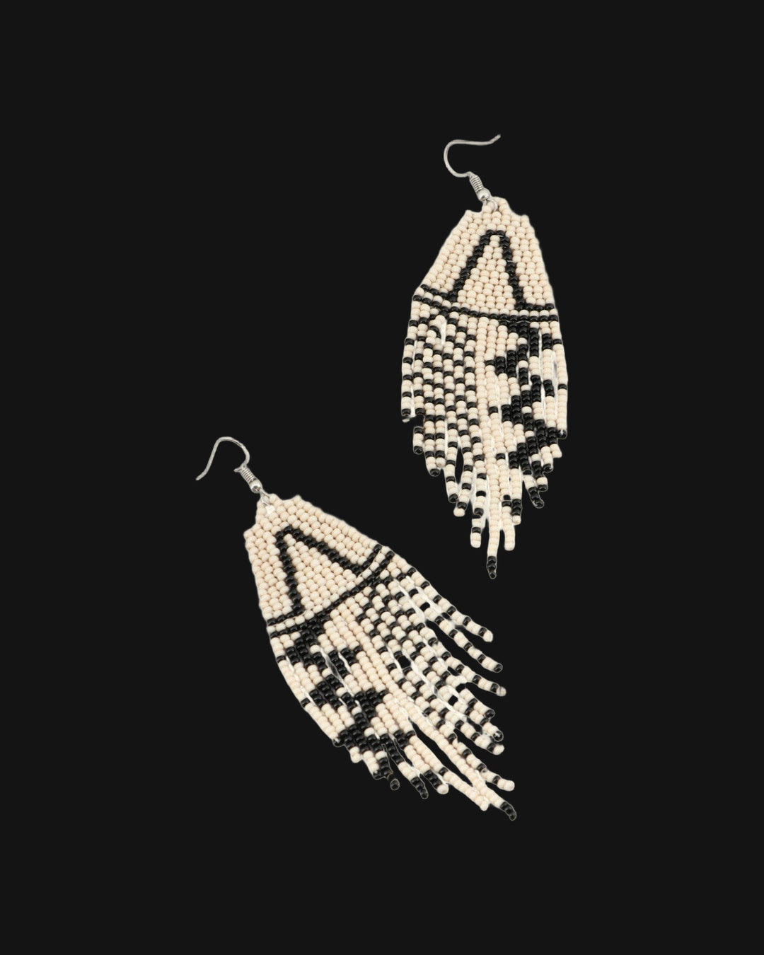 Pair of triangle motif beaded fringe earrings laid diagonally, showing the zigzag black pattern, shown on a black background