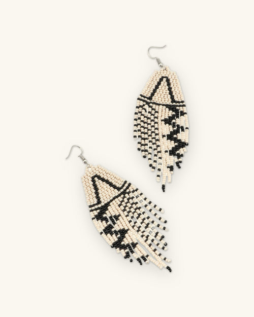 Pair of triangle motif beaded fringe earrings laid diagonally, showing the zigzag black pattern, shown on a sand background