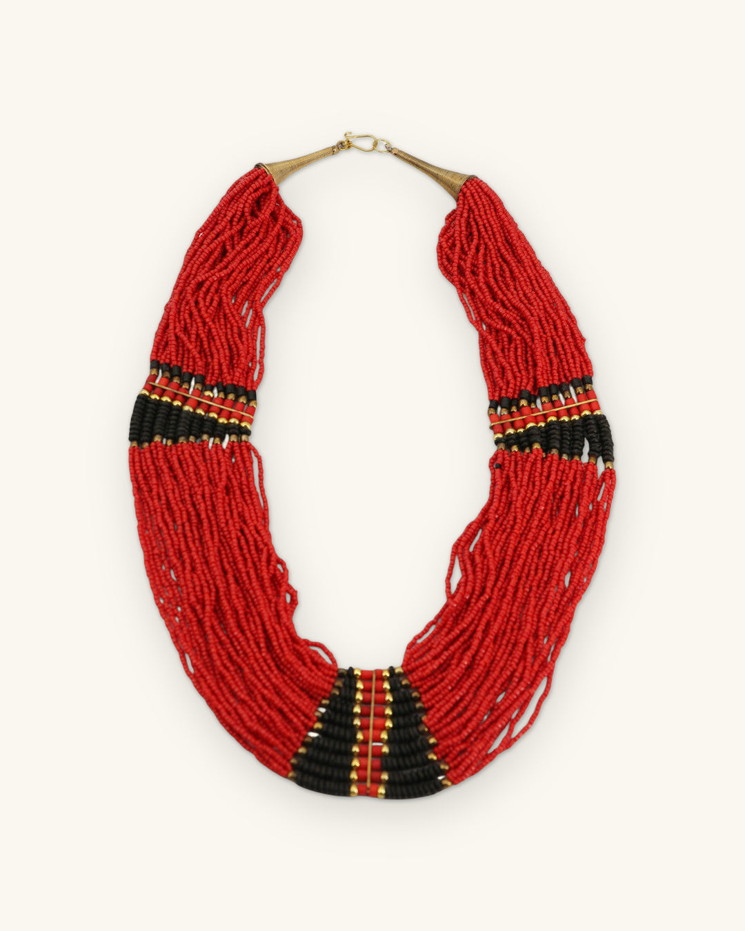 Red seed bead collar necklace with black and gold striped panels and brass cone clasp, full view, shown on a sand background