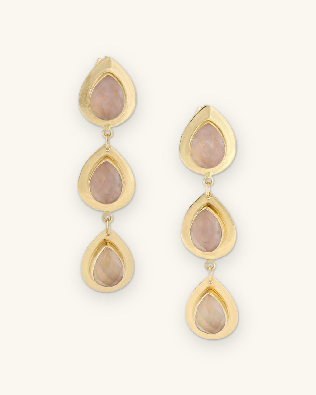 Triple teardrop rose quartz drop earrings in brass bezel settings, made in India, shown on a sand background