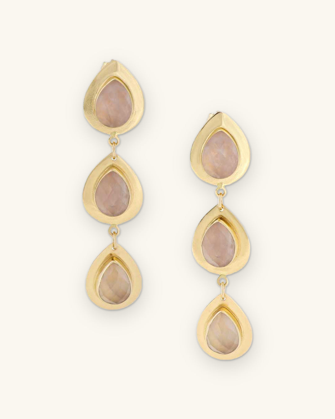 Triple teardrop rose quartz drop earrings in brass bezel settings, made in India, shown on a sand background