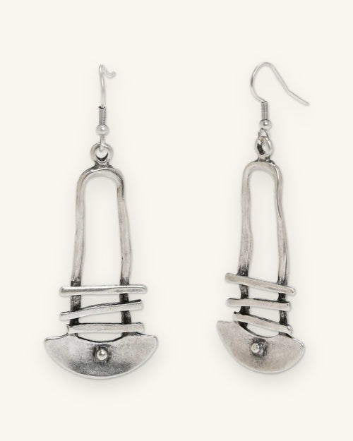 Silver-tone arch earrings with three crossbars and a dotted crescent on fish-hook ear wires, shown on a sand background