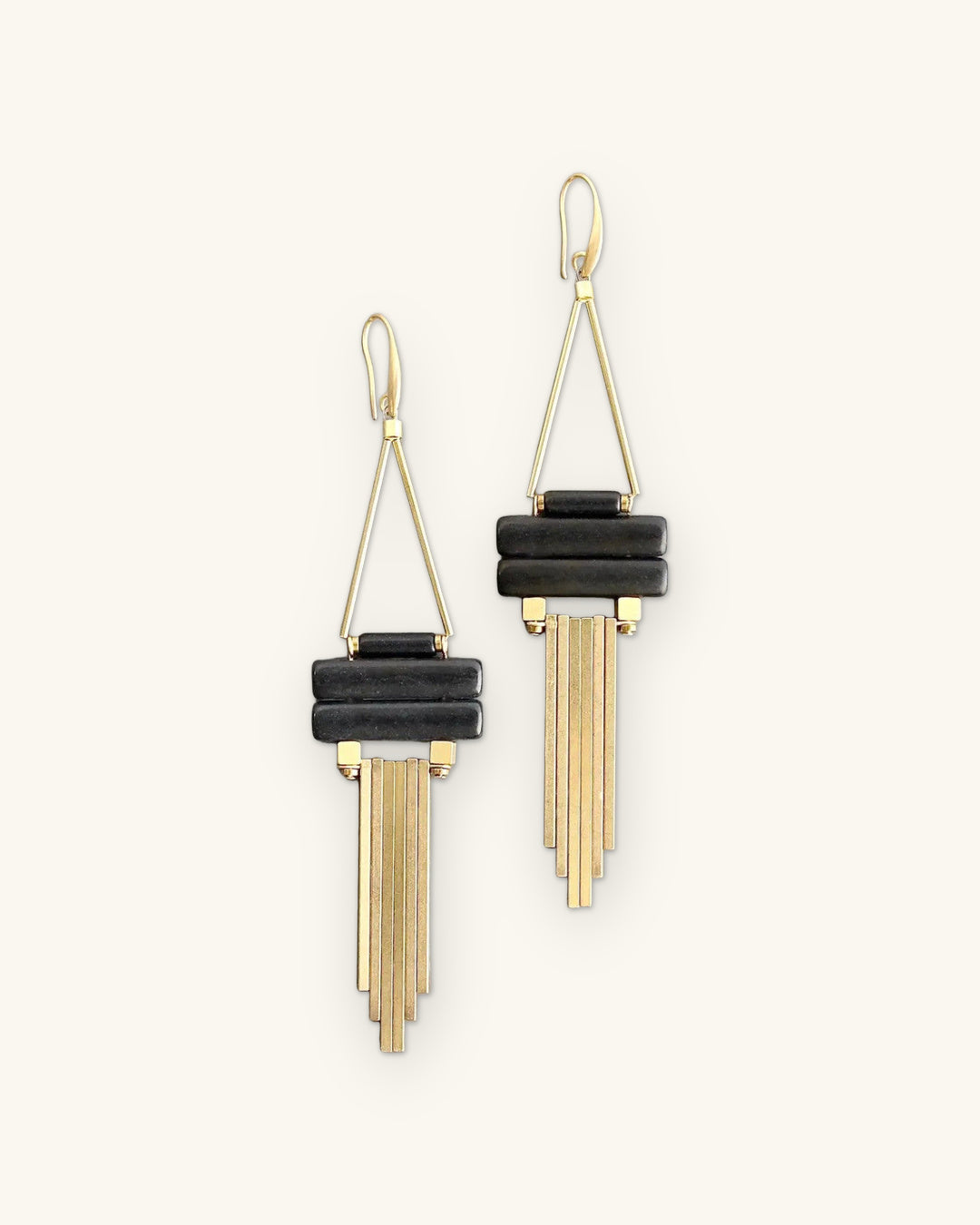 Chandelier earrings with stacked black magnesite bars and gold-plated brass fringe, made in the USA, shown on a sand background