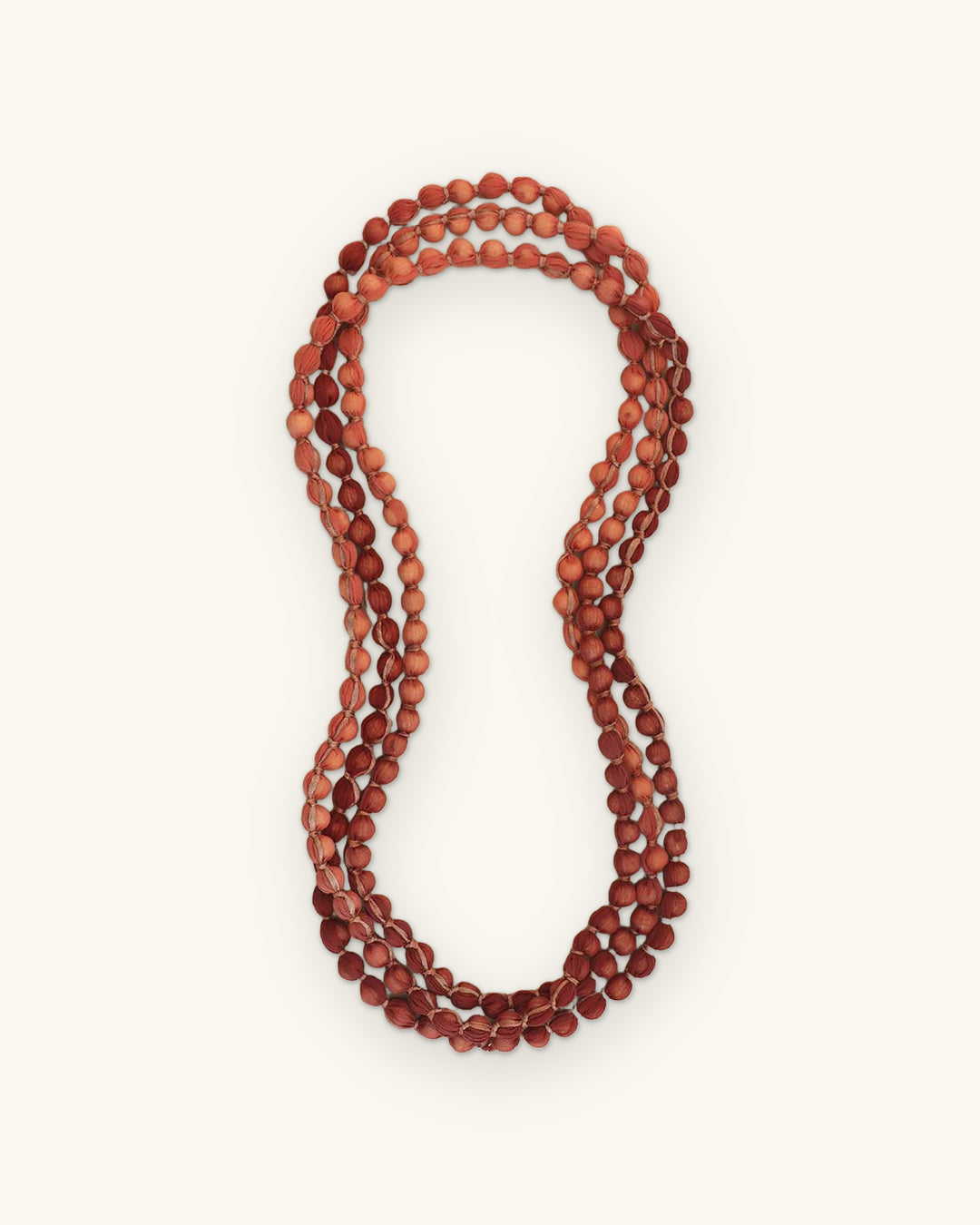 Endless rose and pink fabric bead rope necklace laid out in a figure-eight shape, shown on a sand background