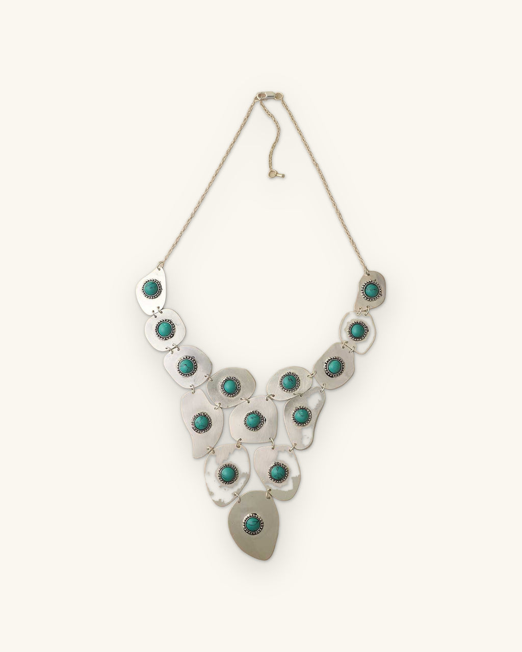 Silver-plated brass freeform plate bib necklace with turquoise polymer clay cabochons, hand-forged in India, shown on a sand background