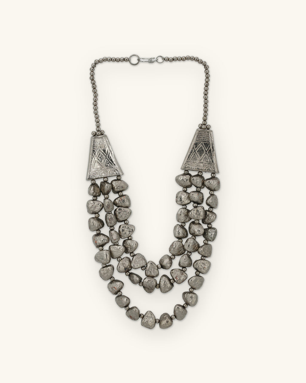 Silver-tone triple-strand nugget necklace with engraved trapezoid cones and ball chain, made in India, shown on a sand background