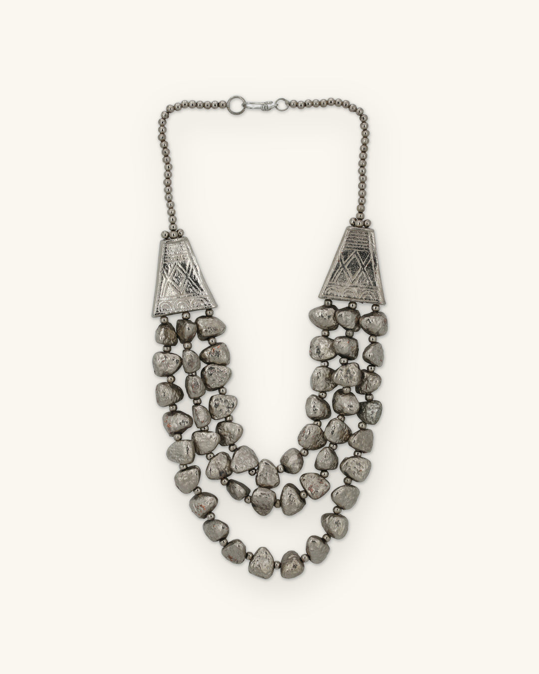 Silver-tone triple-strand nugget necklace with engraved trapezoid cones and ball chain, made in India, shown on a sand background