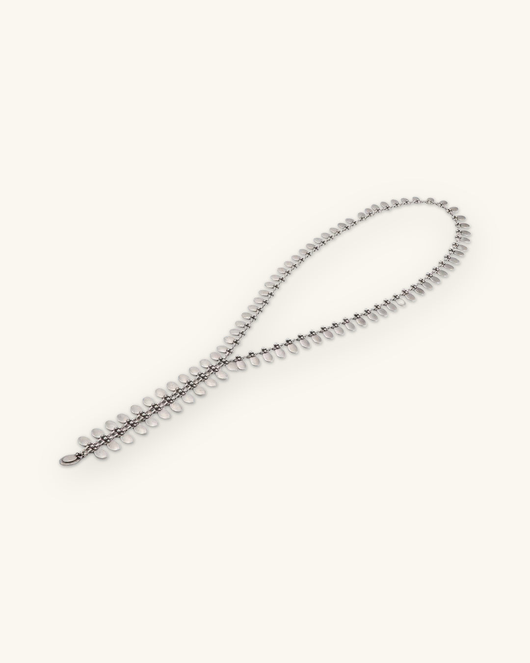 Pewter tab Y-necklace laid in a loose loop showing the row of small oval tabs, shown on a sand background