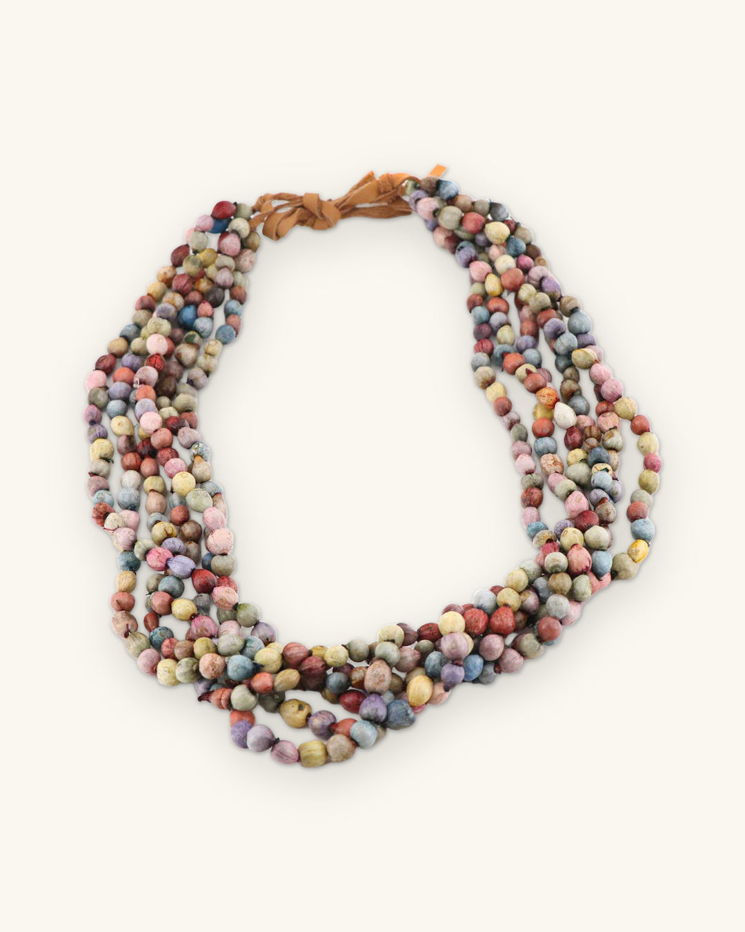 Six-strand multicolor Job's Tears seed bead necklace with suede tie in dusty pink, blue and ochre, made in Uganda, shown on a sand background