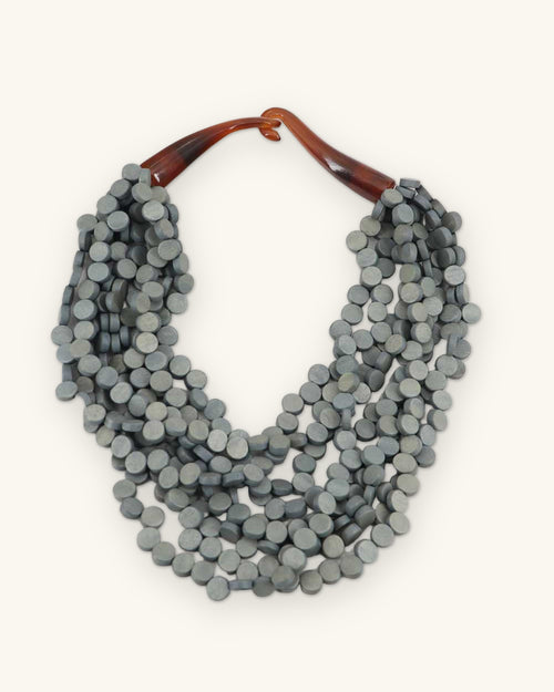 Slate gray dyed wood disc bib necklace with amber horn closure, handmade in the Philippines, shown on a sand background