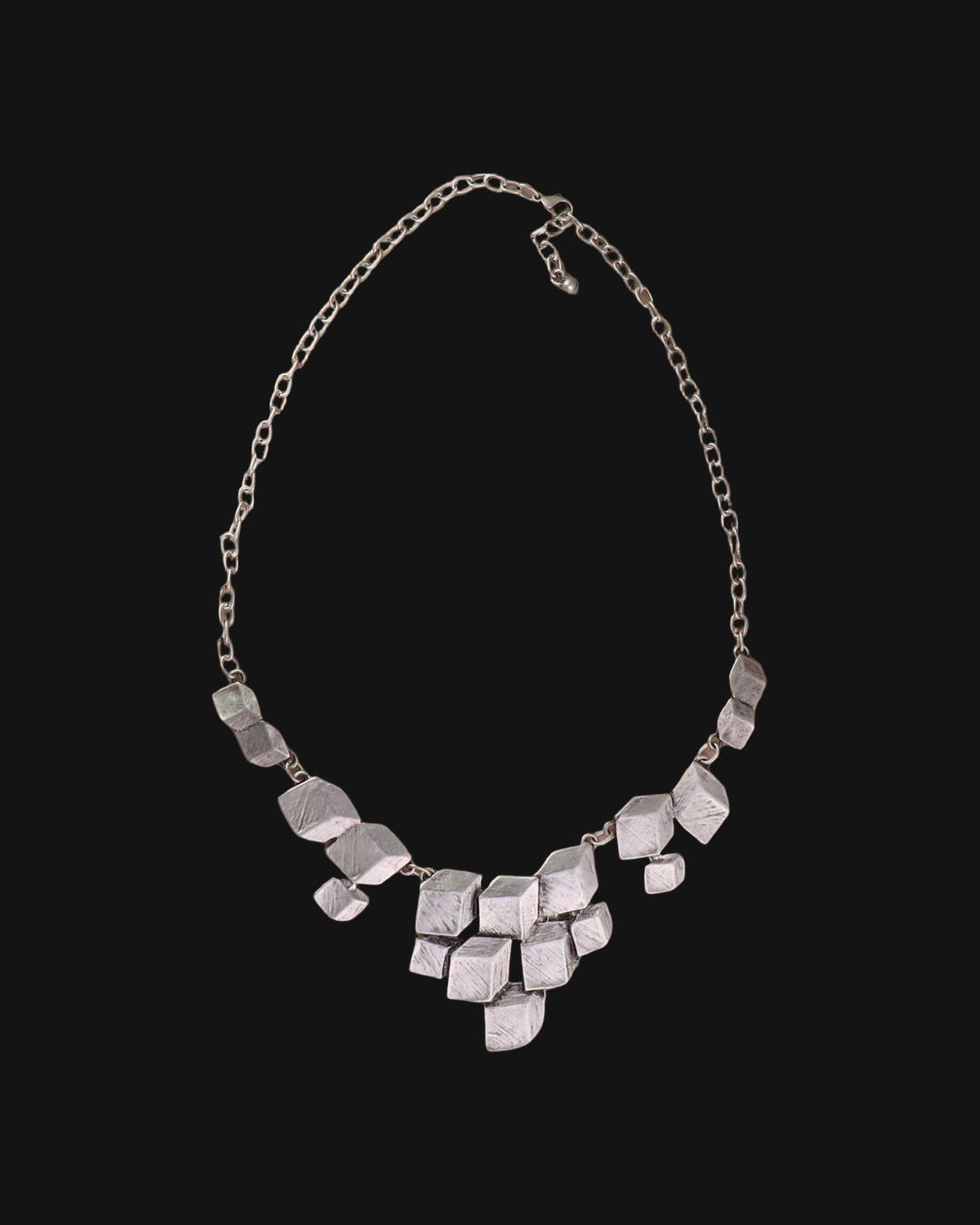 Stacked cube silver necklace with lobster clasp and extender chain laid on a taupe surface, shown on a black background