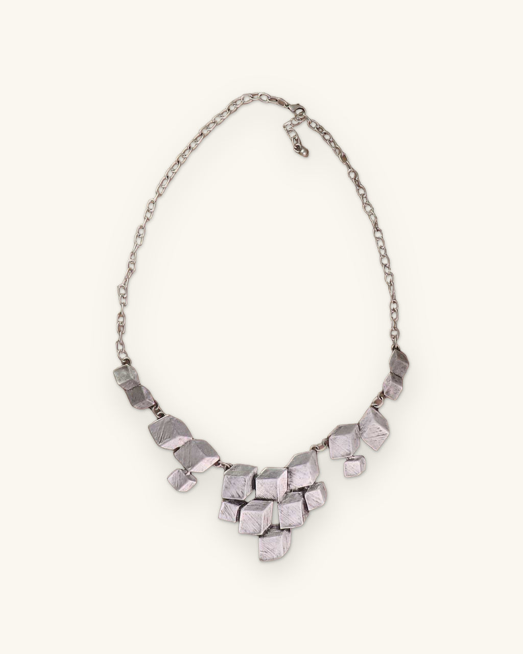 Stacked cube silver necklace with lobster clasp and extender chain laid on a taupe surface, shown on a sand background