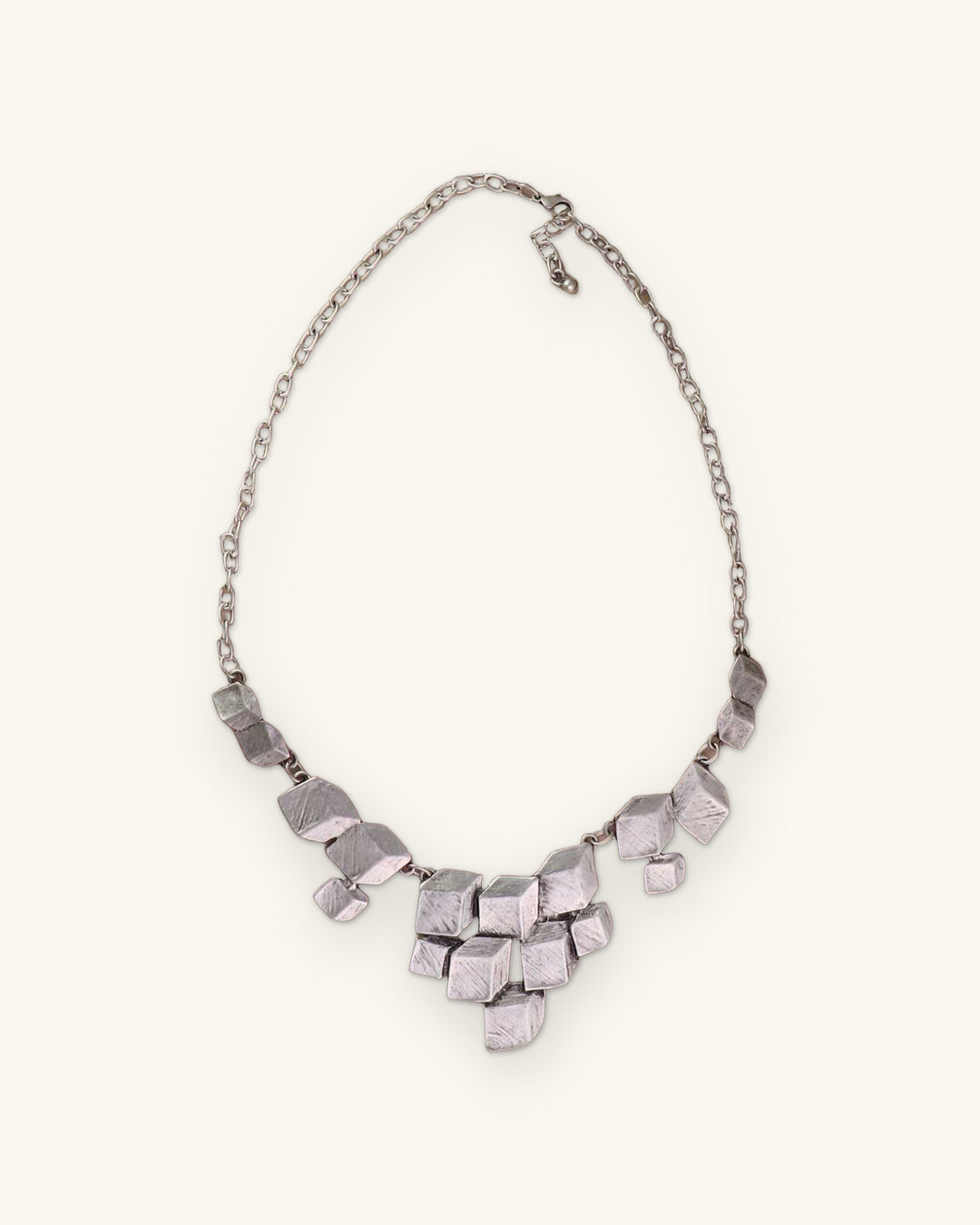 Stacked cube silver necklace with lobster clasp and extender chain laid on a taupe surface, shown on a sand background