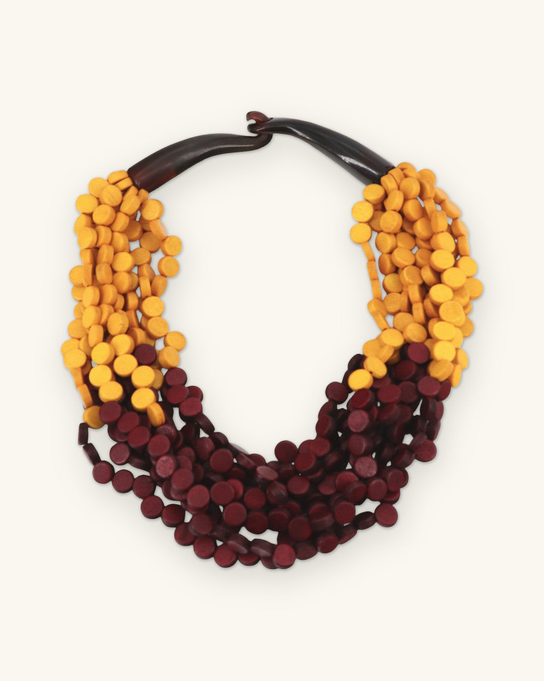 Multi-strand saffron and burgundy wood disc necklace with a curved dark horn closure, shown on a sand background