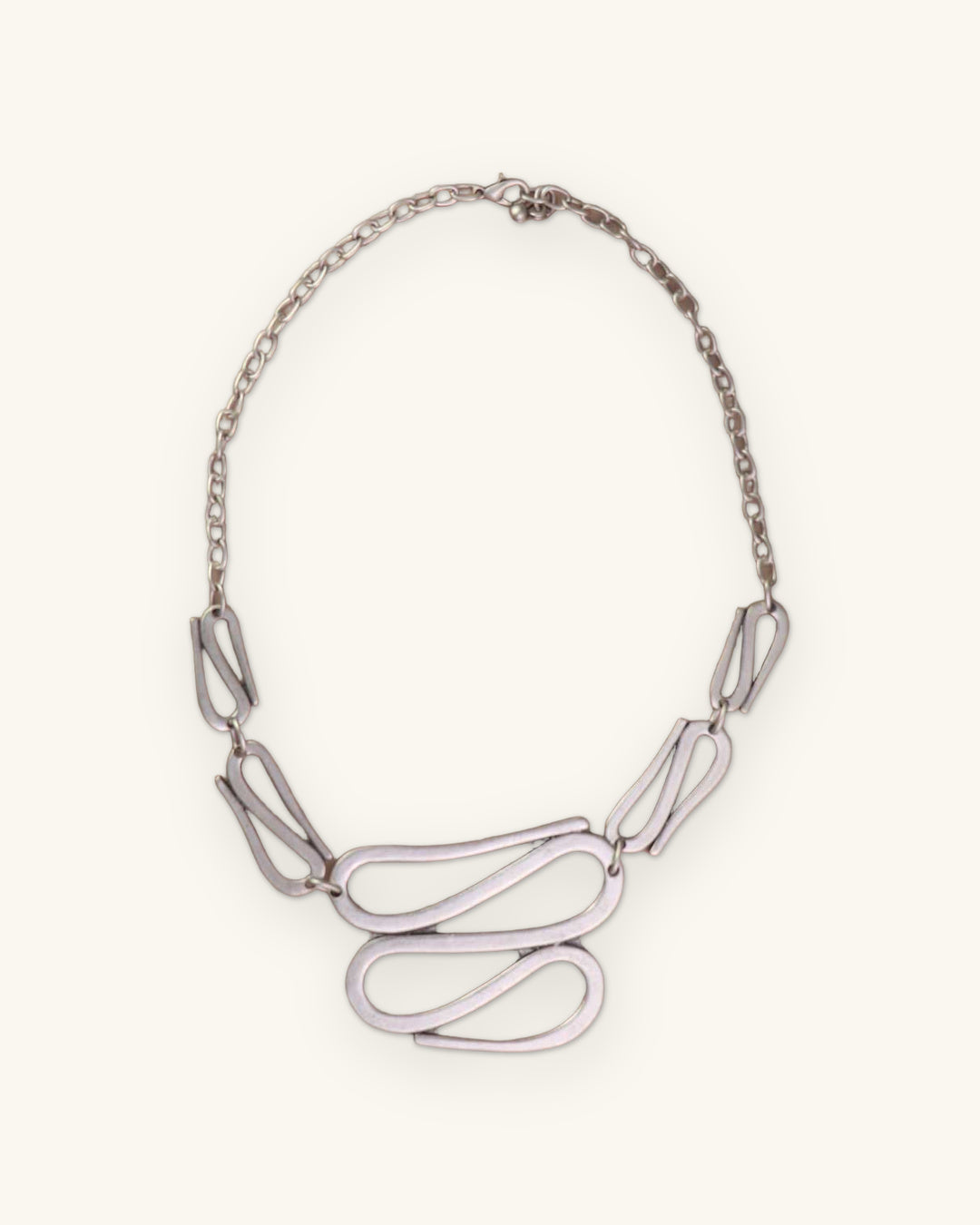 S-curve sculptural necklace with cable chain and lobster clasp laid on a taupe surface, shown on a sand background