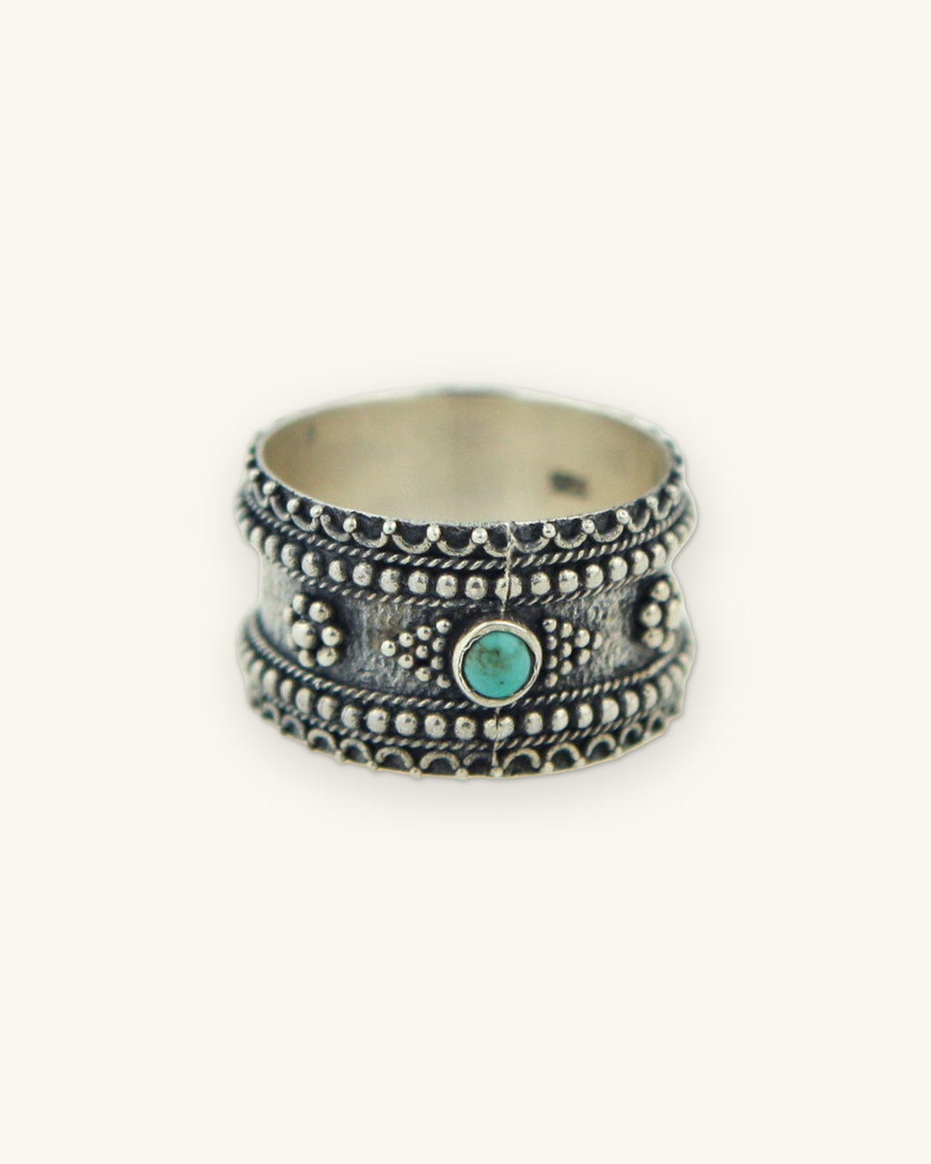Sterling silver granulation band ring with a bezel-set turquoise center stone, made in Thailand, shown on a sand background
