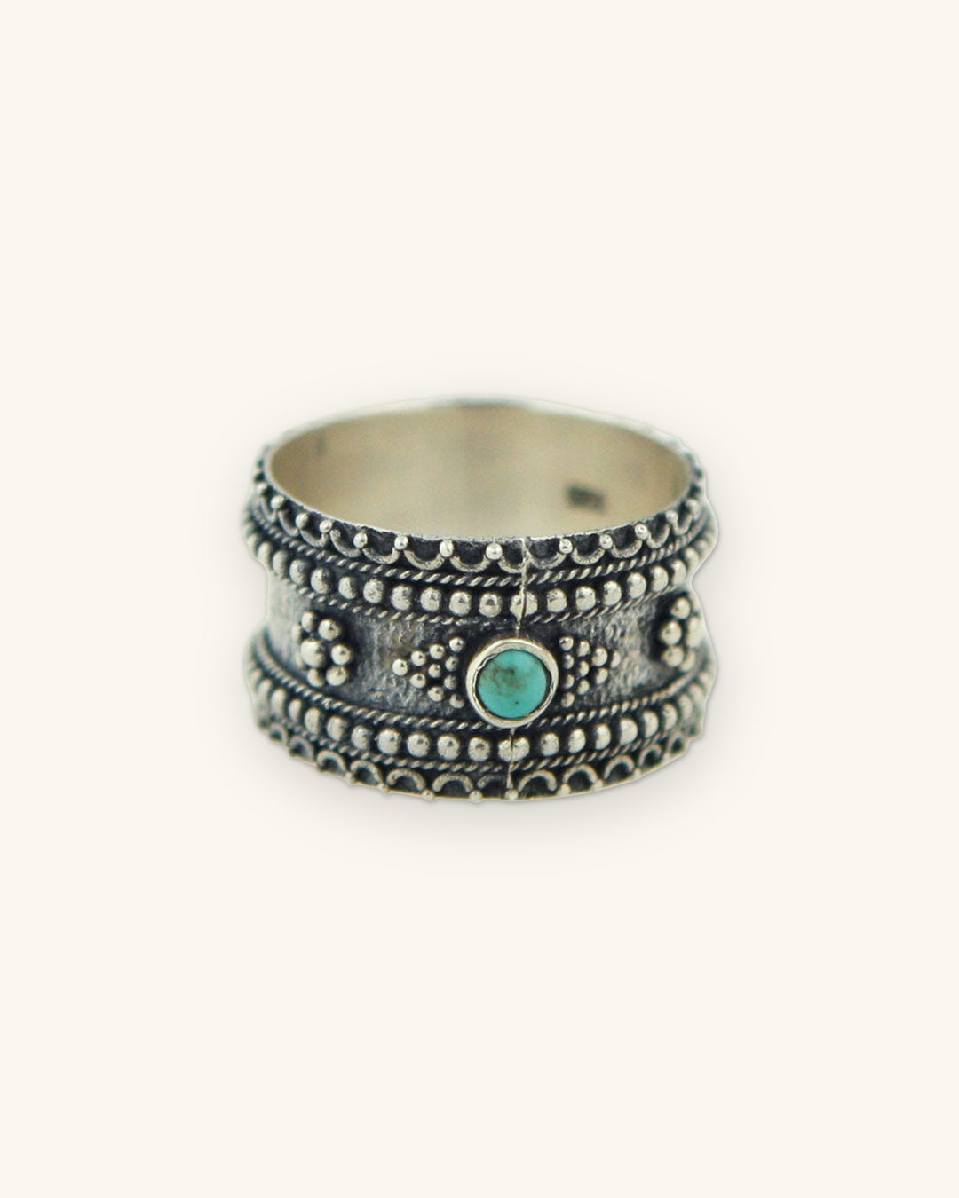 Sterling silver granulation band ring with a bezel-set turquoise center stone, made in Thailand, shown on a sand background