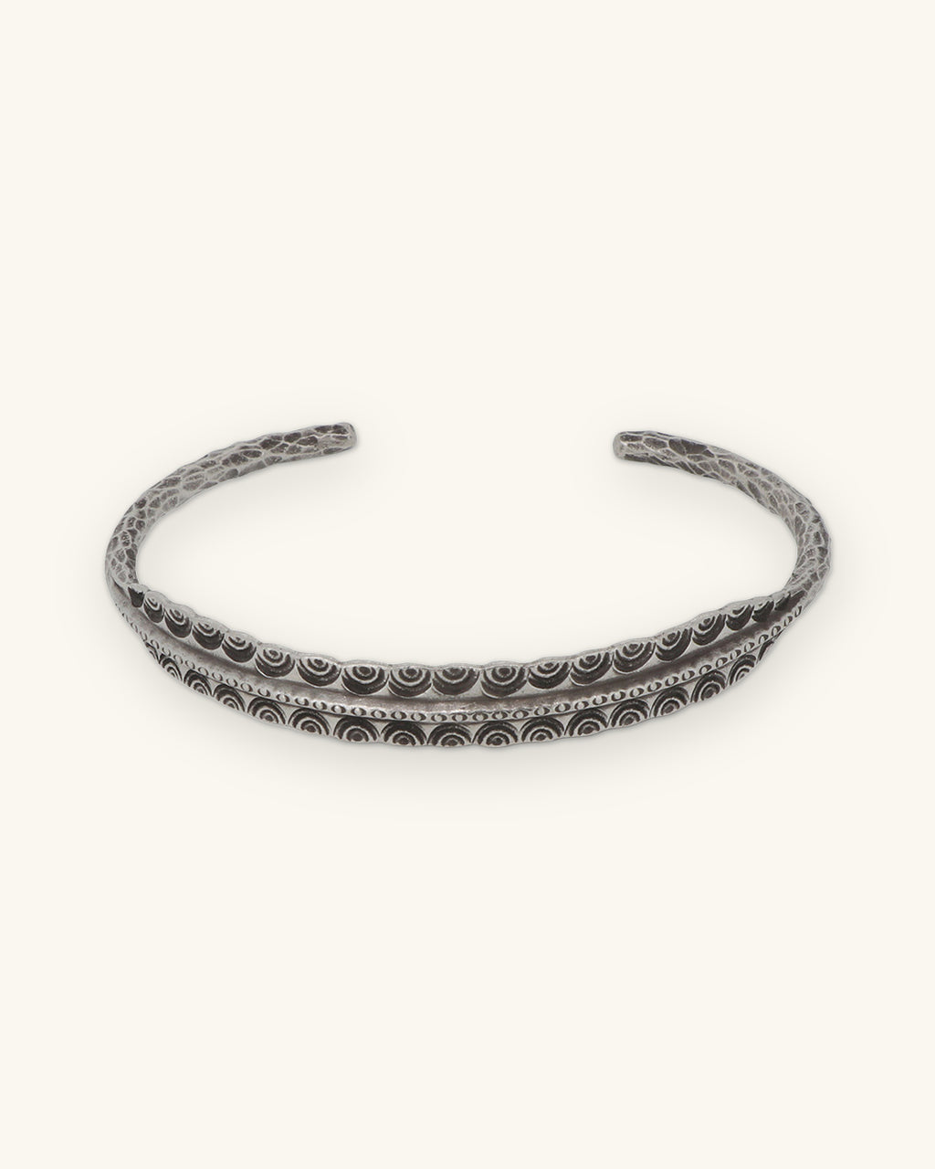 Front view of the open silver cuff with nested arc stamping along the center, shown on a sand background