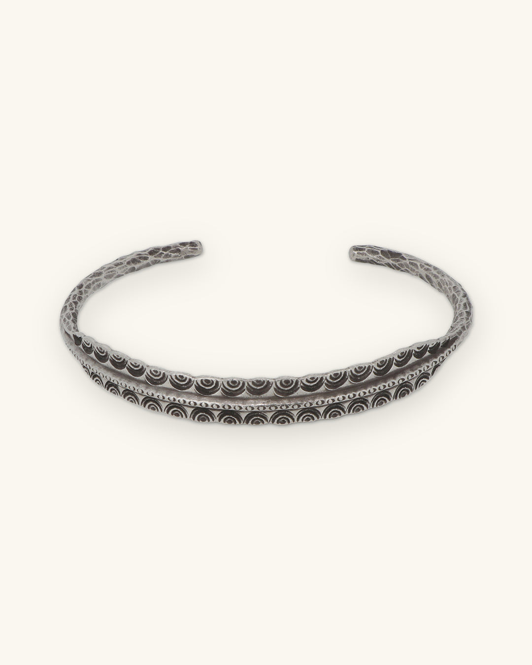 Front view of the open silver cuff with nested arc stamping along the center, shown on a sand background