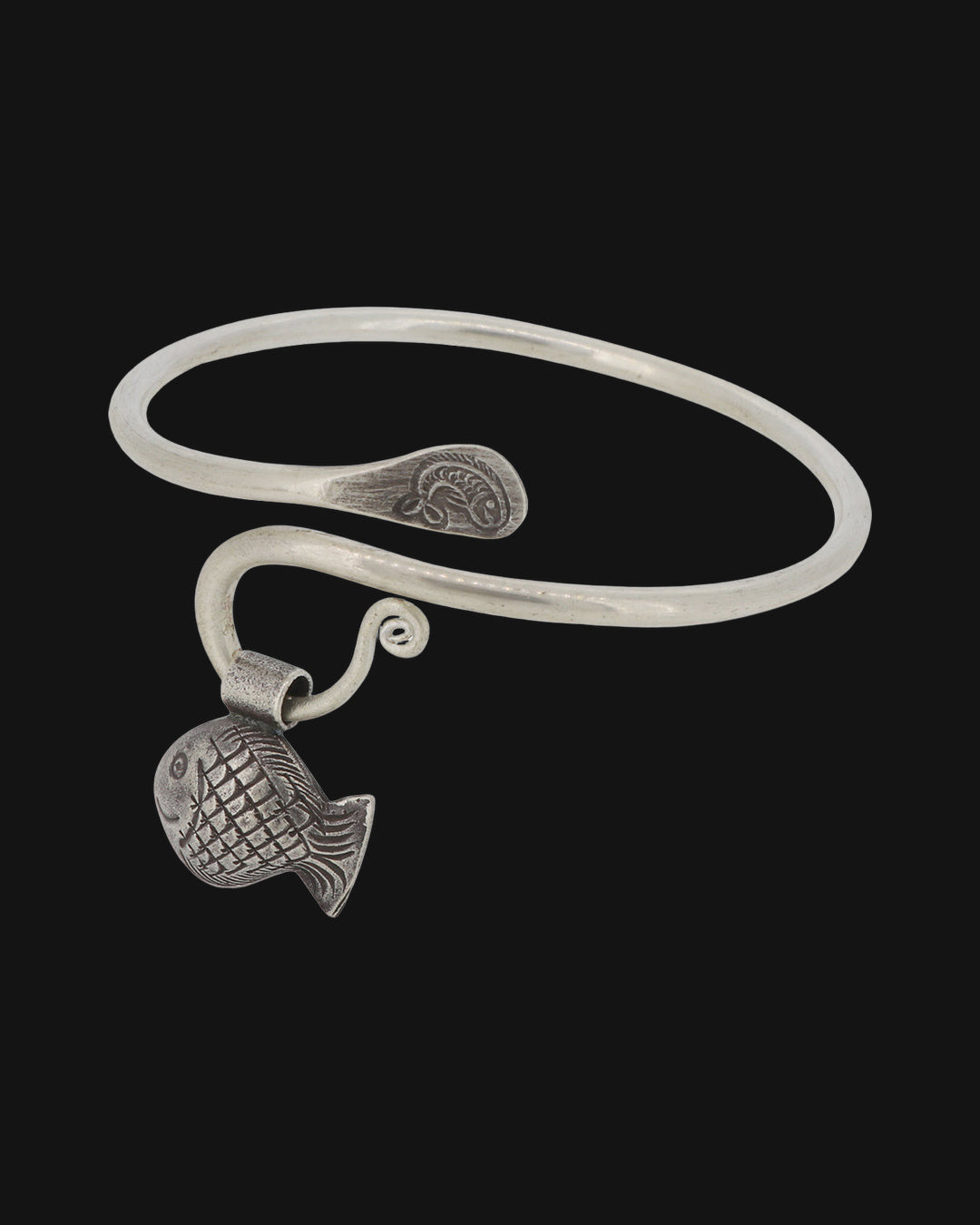 Silver open cuff bracelet with a textured fish charm, stamped spiral ends and curled wire loop, shown on a black background