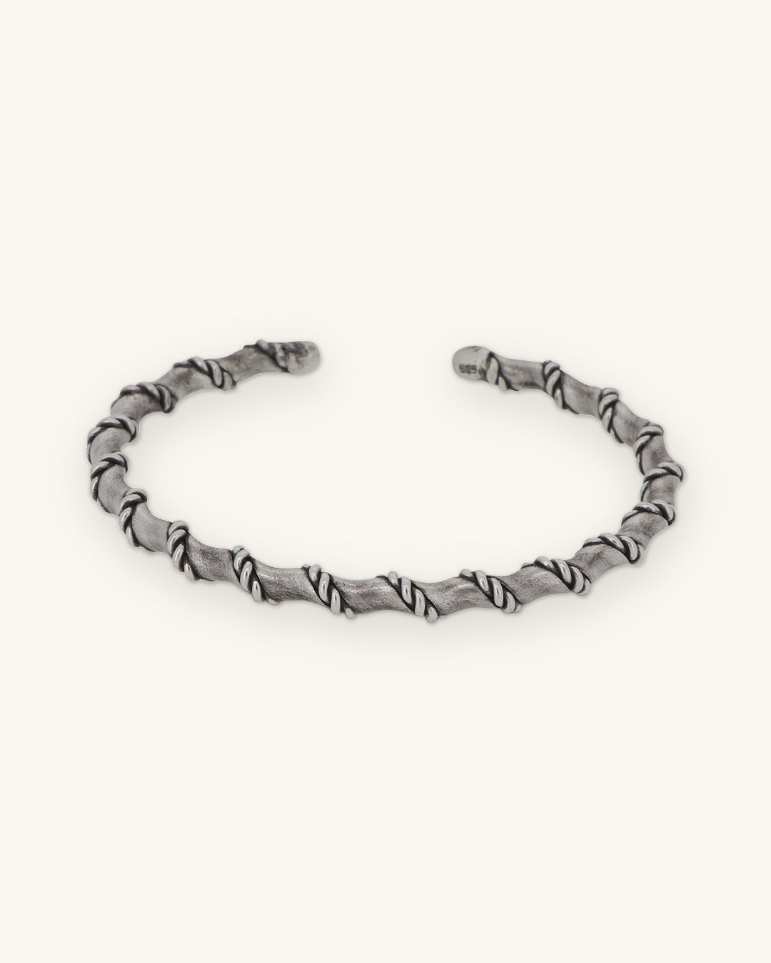 Oxidized sterling silver open cuff wrapped in a rope spiral, front view, shown on a sand background