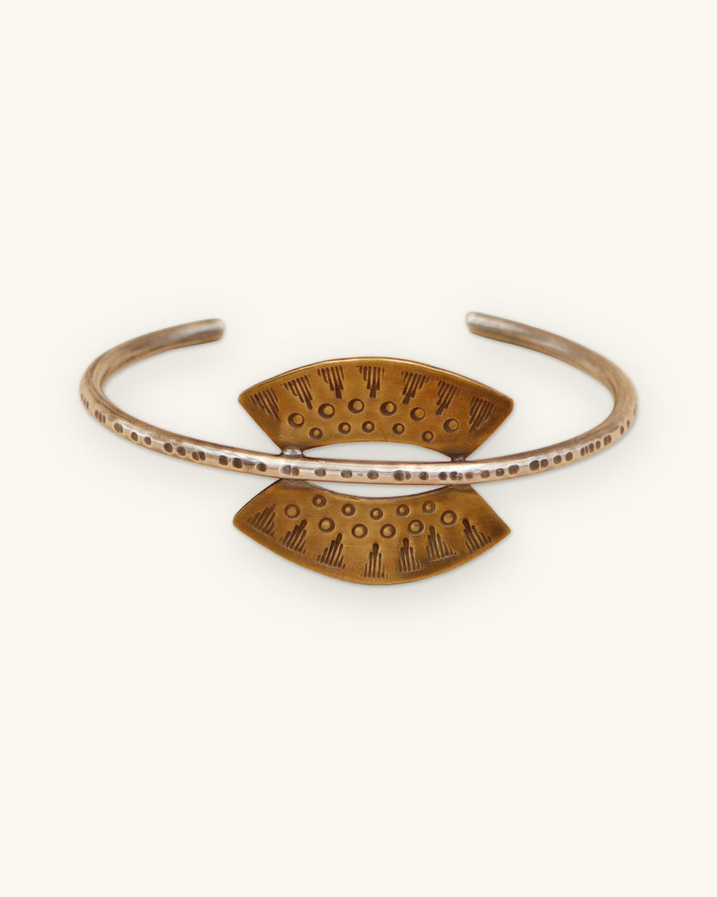 Hand-stamped brass sun cuff on an oxidized sterling silver band, made in the USA, shown on a sand background