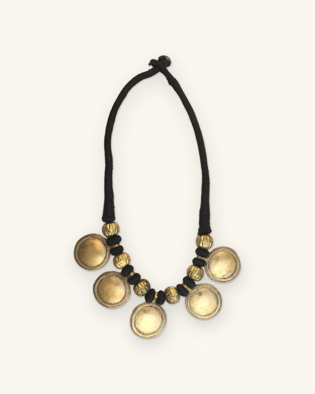 Domed disc necklace on black cord worn with a pale yellow blazer, shown on a sand background