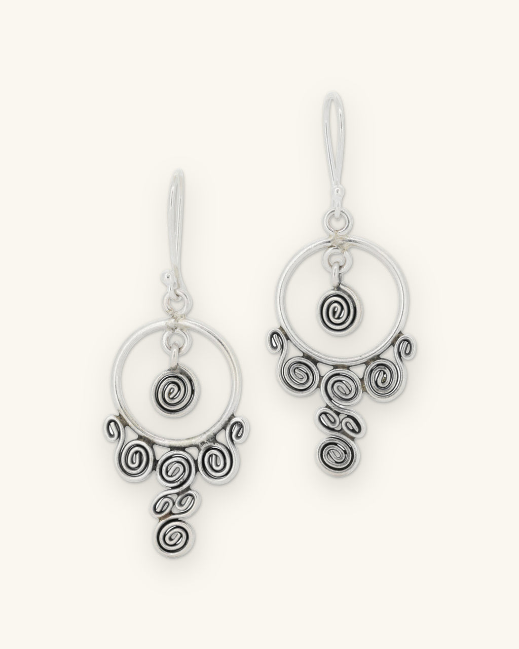 Silver chandelier earrings with an open hoop, center spiral and cascading coiled spirals, front view, shown on a sand background