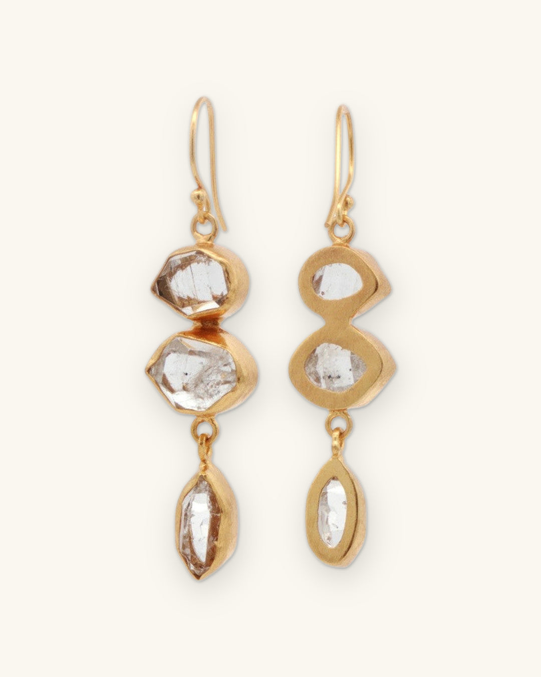 Herkimer quartz drop earrings, one turned to show the open-backed gold bezels, shown on a sand background