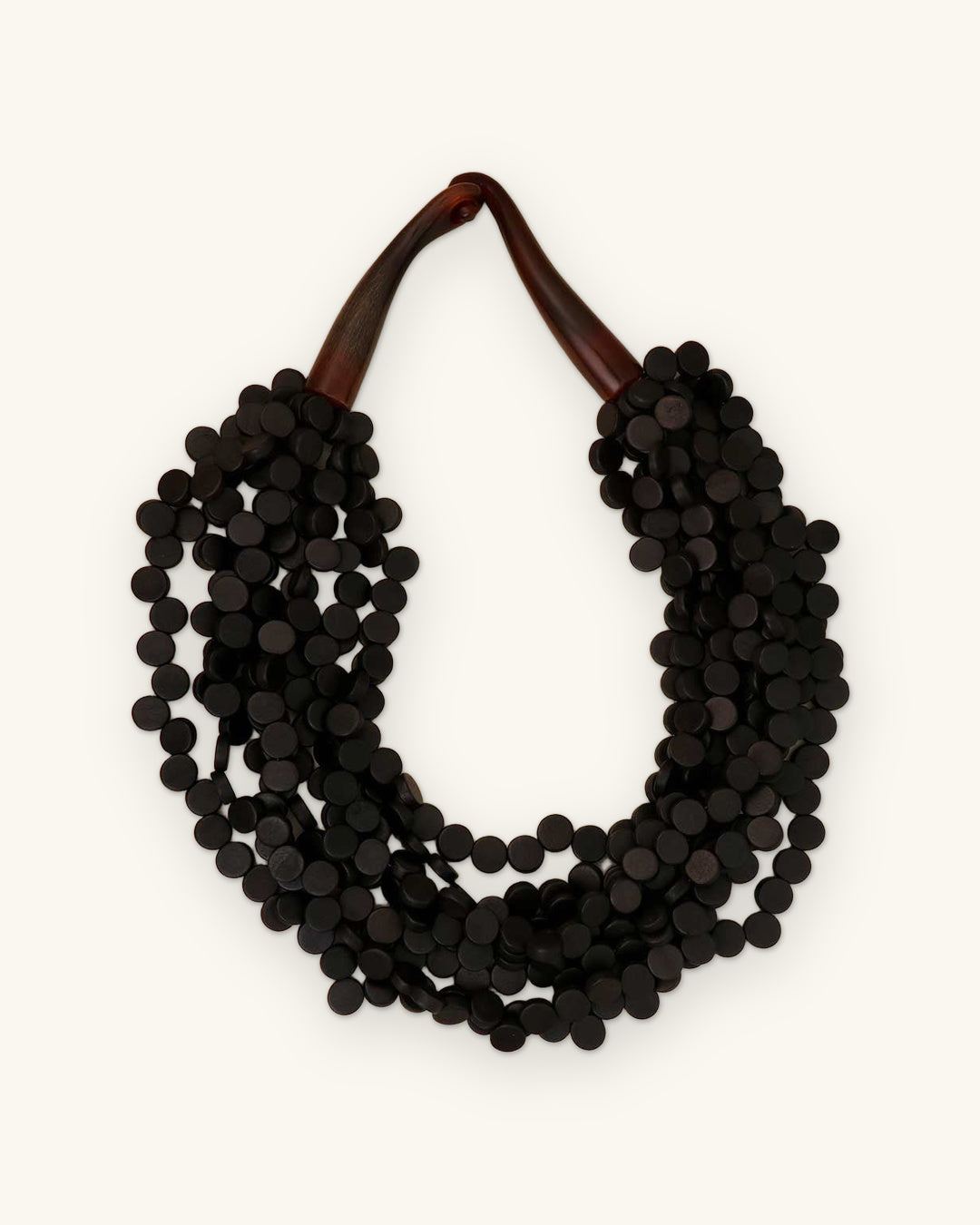 Black wood disc multi-strand collar necklace with polished brown horn closure, made in the Philippines, shown on a sand background