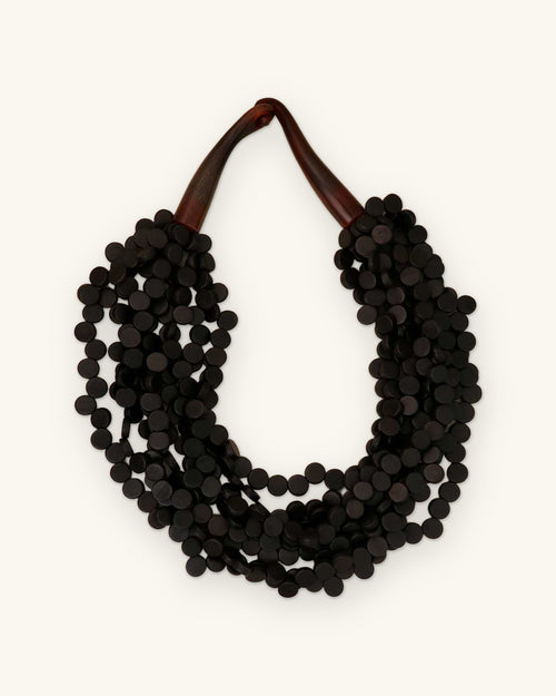 Black wood disc multi-strand collar necklace with polished brown horn closure, made in the Philippines, shown on a sand background