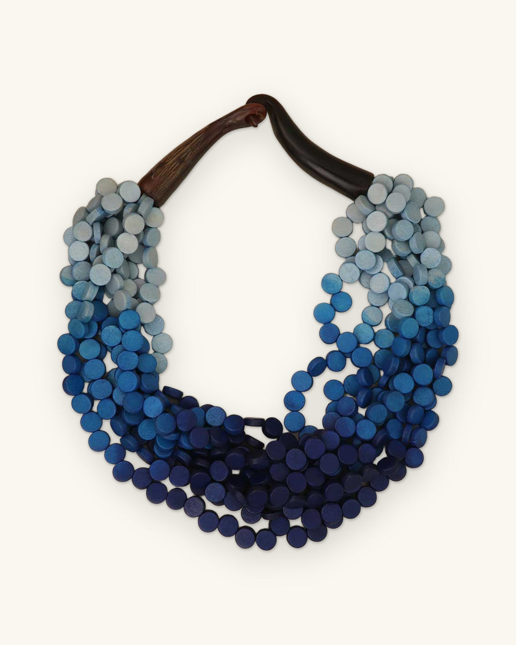 Indigo gradient wood disc bib necklace shading from pale blue to navy with a horn closure, from the Philippines, shown on a sand background