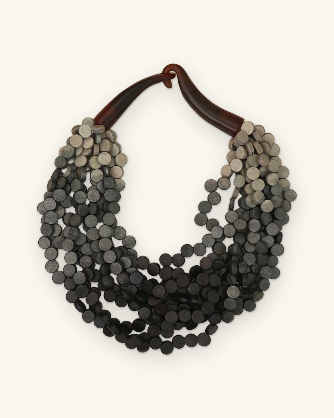 Gray ombré wooden disc multi-strand necklace fading to charcoal with a horn closure, from the Philippines, shown on a sand background