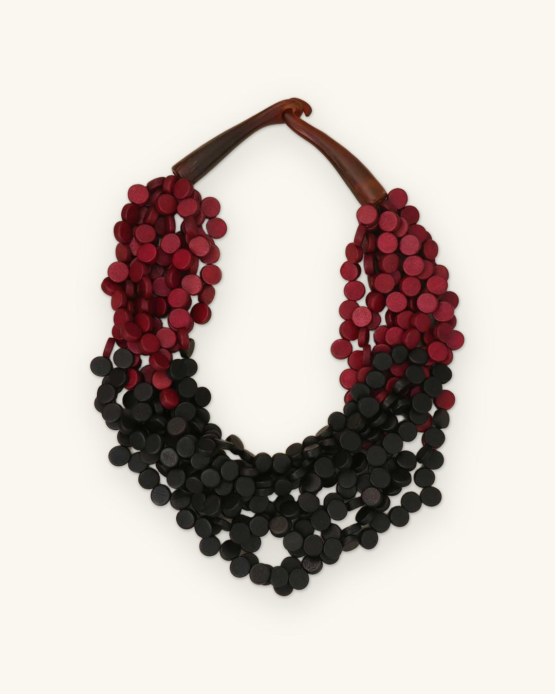 Twisted multi-strand wood disc necklace in red and black with carved horn closure, made in the Philippines, shown on a sand background