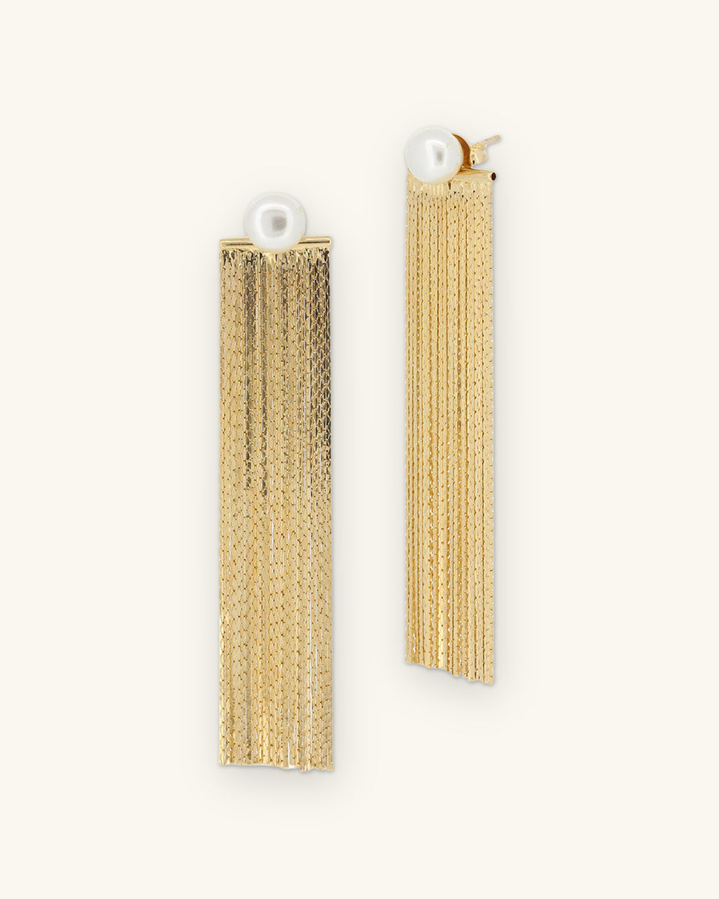 Gold-plated brass chain fringe earrings with detachable pearl studs, made in Brazil, front view, shown on a sand background