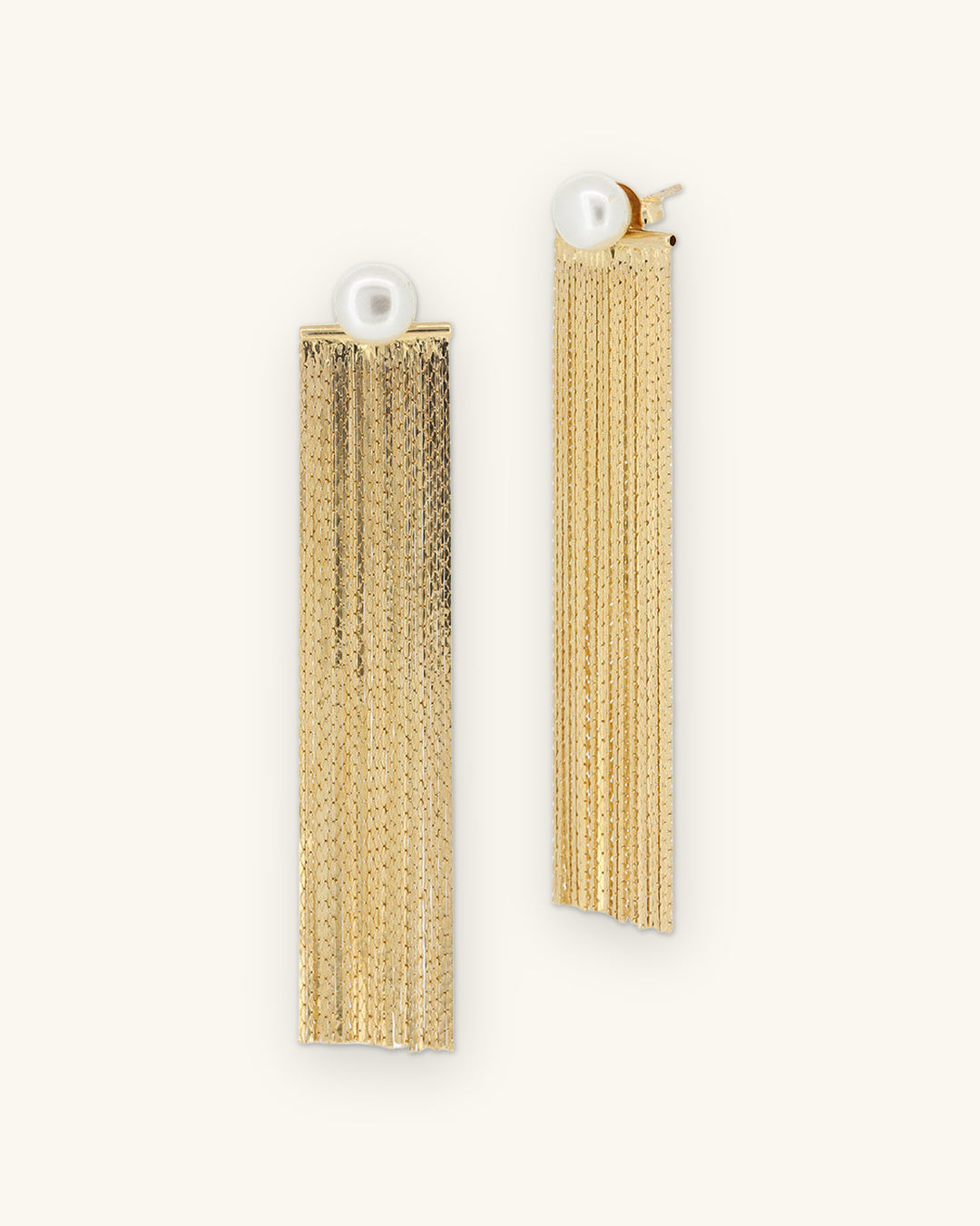 Gold-plated brass chain fringe earrings with detachable pearl studs, made in Brazil, front view, shown on a sand background